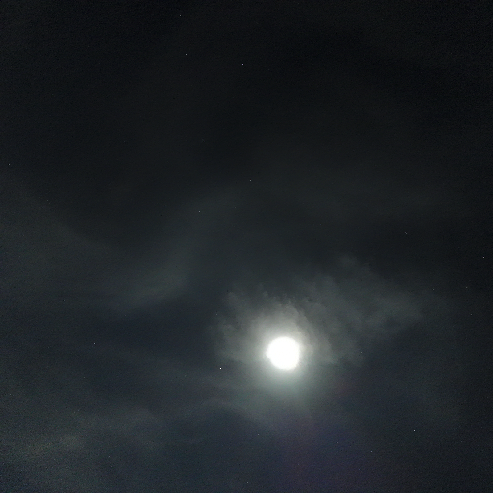 The Moon breaking through drifting clouds, edges lit silver by moonlight, over a dark Minnesota sky